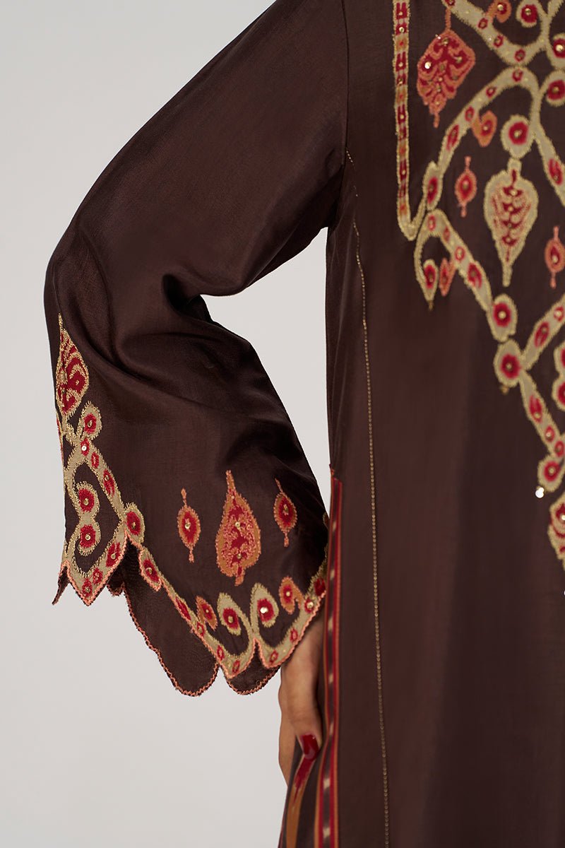 Close-up of a dark brown traditional embroidered garment with ornate red and beige floral embroidery on the sleeve cuff and side panel, shown against a light gray studio background. | Deep Coffee Festive Co-ord Set - Ganga Fashions