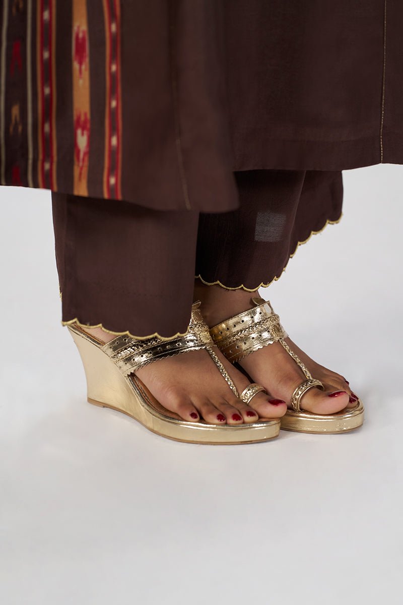 A close-up of a person's feet wearing metallic gold wedge sandals with embellished straps, paired with dark brown traditional pants against a light gray studio background. | Deep Coffee Festive Co-ord Set - Ganga Fashions