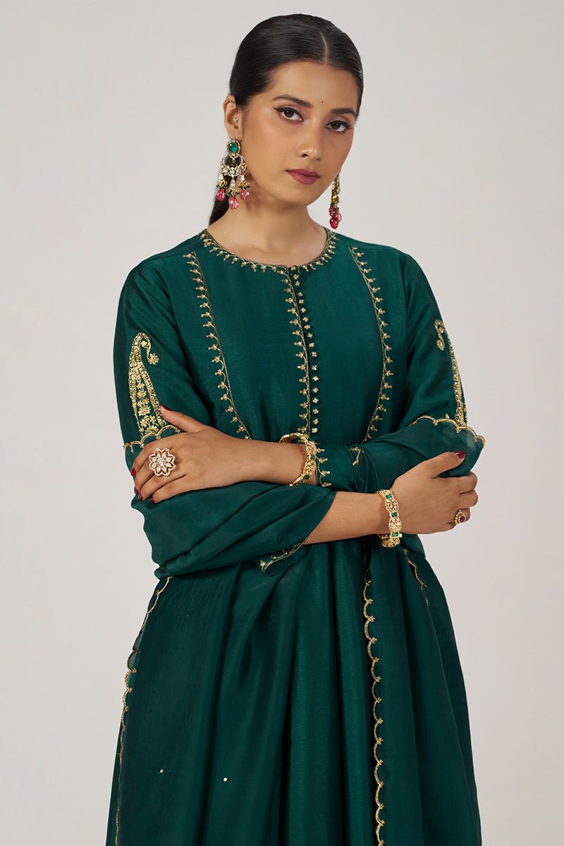 A woman modeling a dark green traditional outfit with gold embroidery, standing against a light gray studio background. | Emerald Green Raw Silk Festive Kurta Set - Ganga Fashions