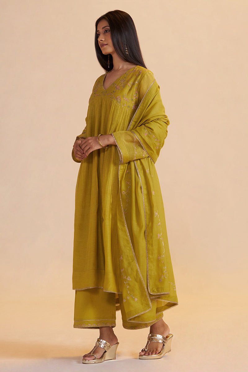 A woman modeling a mustard yellow traditional outfit with matching pants and a draped dupatta, featuring subtle embroidery and gold-toned wedge sandals, set against a solid beige studio background. | Lemon Curry Festive Kurta Set - Ganga Fashions