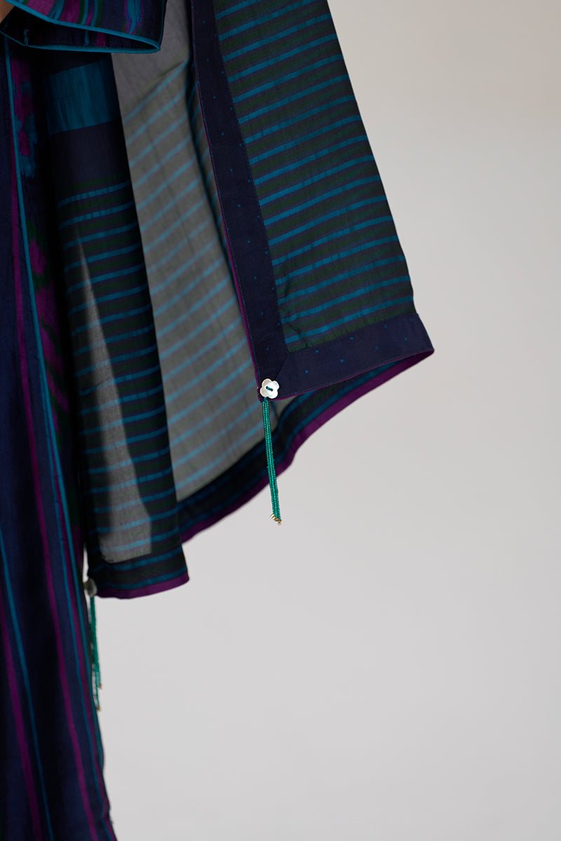 A close-up of a patterned garment or fabric panel with dark navy, teal, and gray striped sections, a solid navy border, and a small hanging green tassel against a plain light background. | Medieval Blue Silk Festive Kurta Set - Ganga Fashions