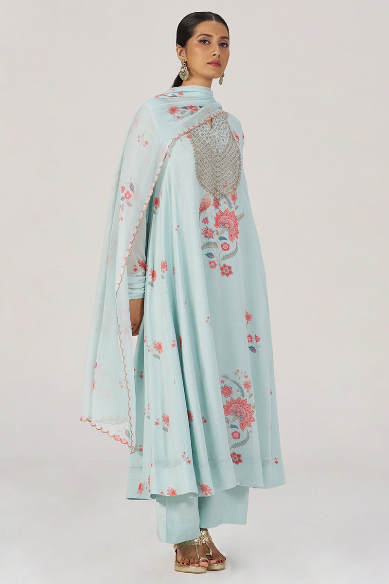A woman modeling a light blue traditional outfit with pink floral embroidery and a matching sheer dupatta, photographed against a plain light gray studio background. | Whispering Blue Georgette Festive Kurta Set - Ganga Fashions