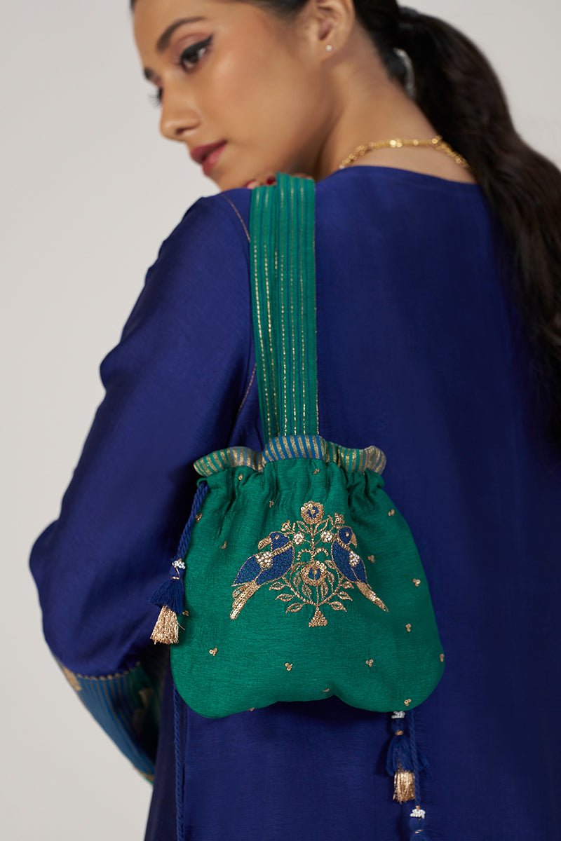 A woman in a royal blue kurta carries a small green embroidered drawstring pouch bag with a wide strap and a peacock motif. | Space Blue Festive Kurta Set - Ganga Fashions
