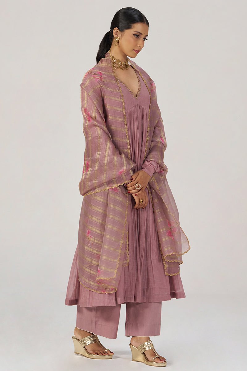 A woman modeling a dusty rose pink traditional outfit with a matching sheer dupatta featuring gold stripes and pink floral accents, set against a plain light gray studio background. | Woodrose Chanderi Silk Festive Kurta Set - Ganga Fashions