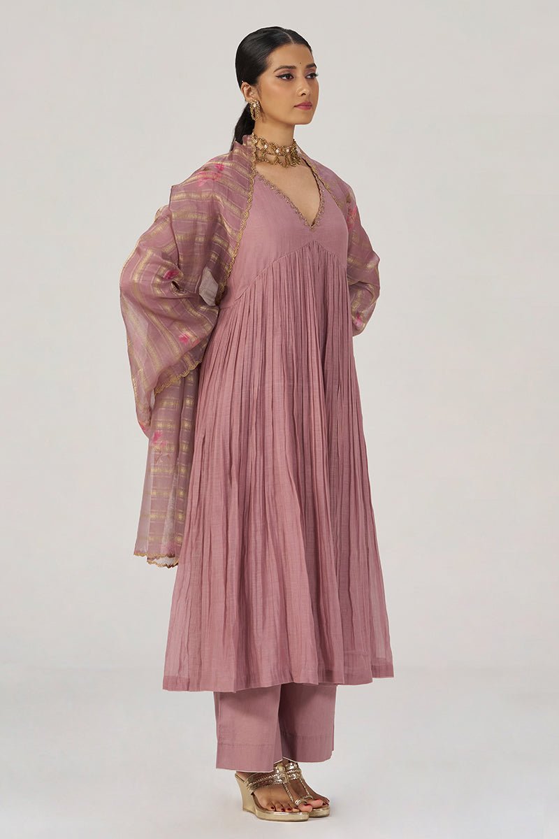 A woman models a dusty pink traditional outfit consisting of a long pleated kurta, matching trousers, and a sheer patterned dupatta, set against a plain light gray studio background. | Woodrose Chanderi Silk Festive Kurta Set - Ganga Fashions
