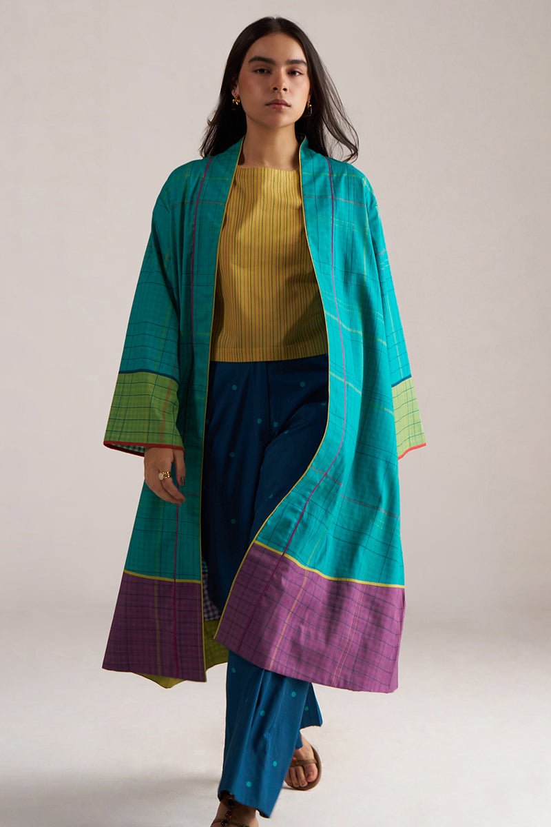 Woman wearing a long turquoise and purple coat over a yellow top and blue pants on a white background | Navigate Blue Checkard Kimono with Moss Yellow Top and Blue Bottom Co Ord Set