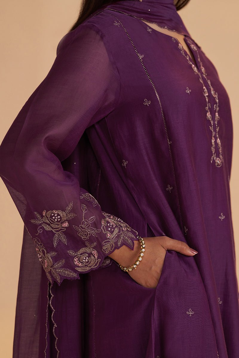A close-up of a person wearing a purple traditional outfit with floral embroidered sleeves and silver mirror-work detailing on a beige background. | Purple Festive Kurta Set - Ganga Fashions