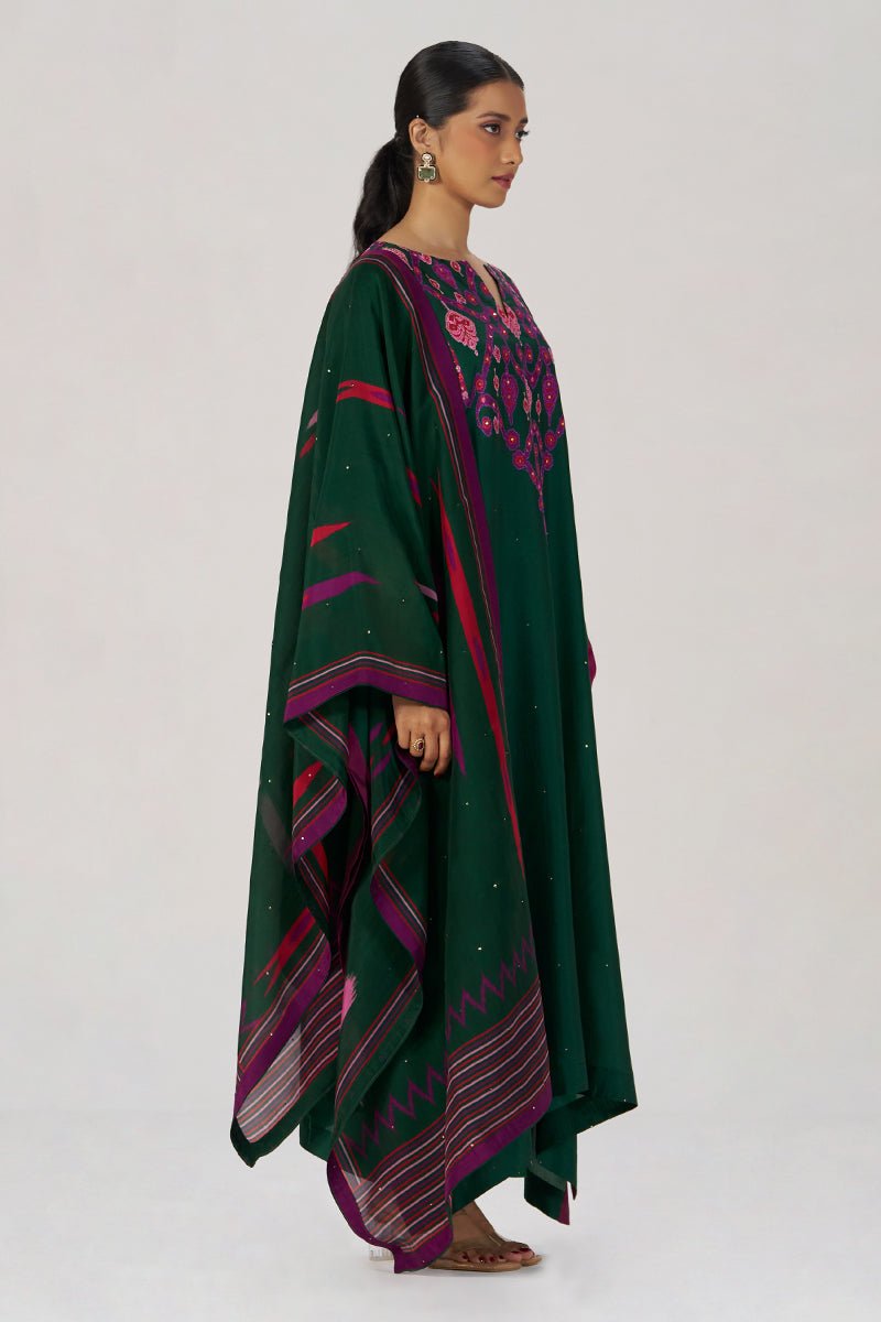 A woman modeling a dark green traditional outfit with pink and purple geometric border patterns and floral embroidery on the neckline, photographed against a plain light gray studio background. | Evergreen Silk Festive Kaftaan Set - Ganga Fashions