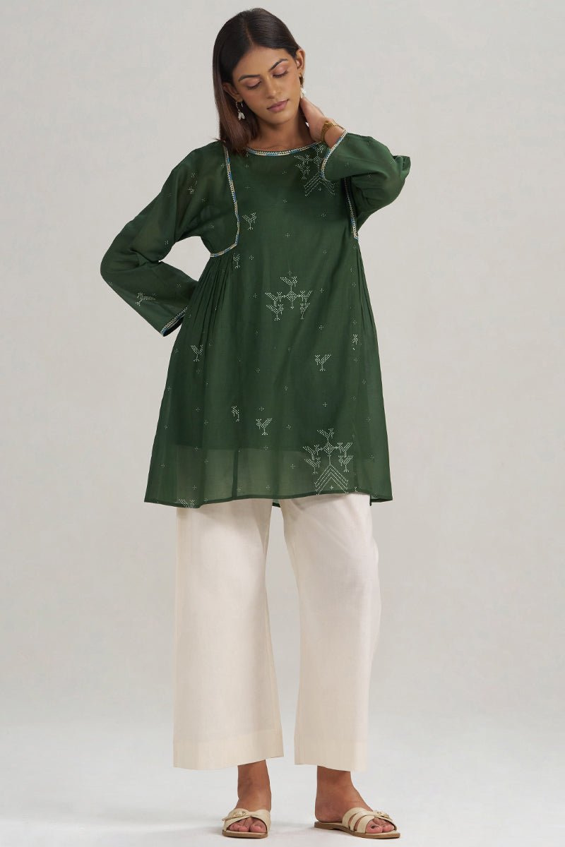 A woman modeling a dark green long-sleeve kurta with subtle white printed motifs, paired with off-white wide-leg pants and beige flat sandals, against a plain light gray studio background. | Mehndi Green Hand-Printed Mul-Mul Tunic - Ganga Fashions