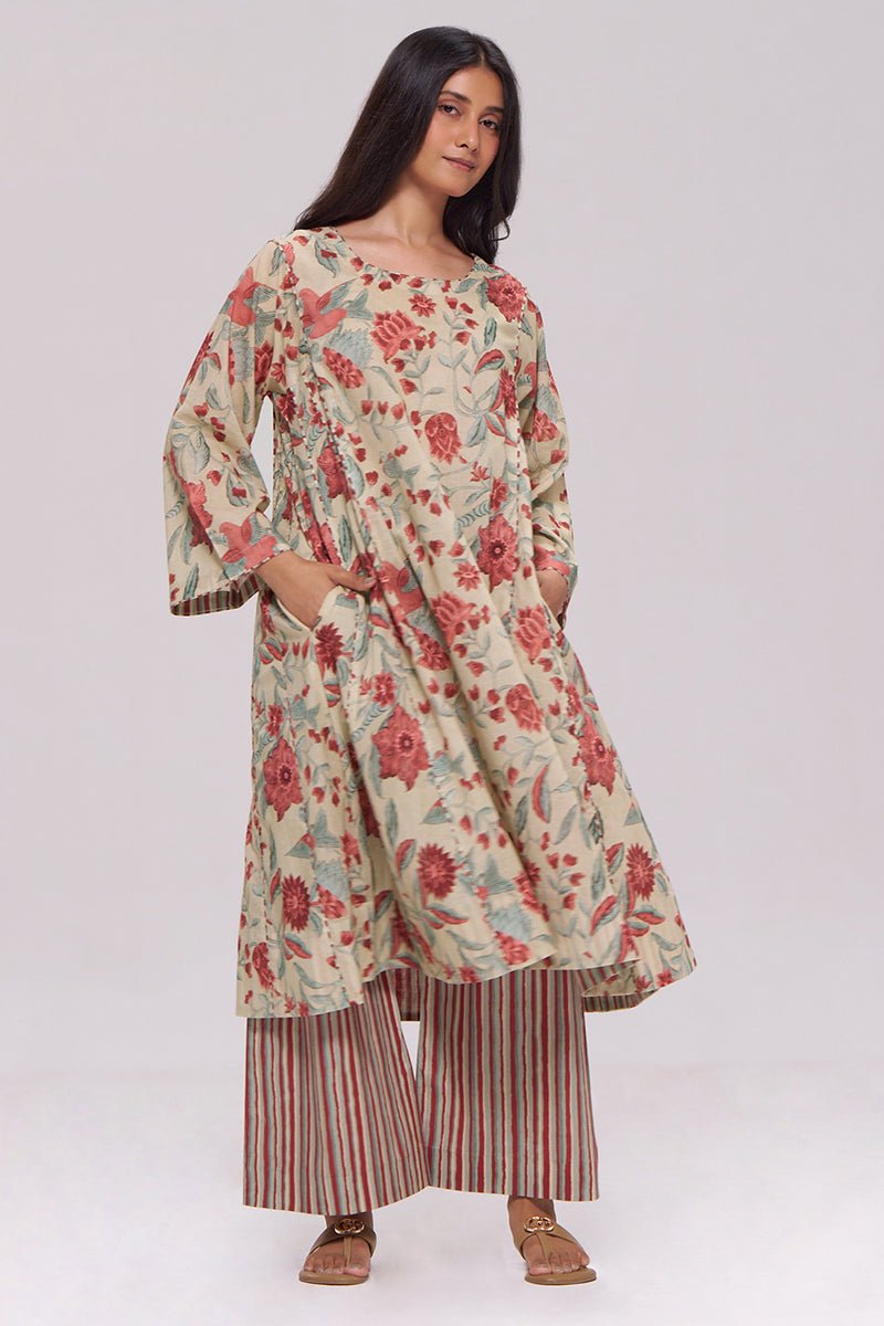 A woman modeling a long-sleeved cream-colored kurta with a red and green floral block print, paired with striped palazzo pants, against a plain light gray studio background. | Vintage Beige and Rose Floral Print Kurta and Stripe Bottom Set - Ganga Fashions