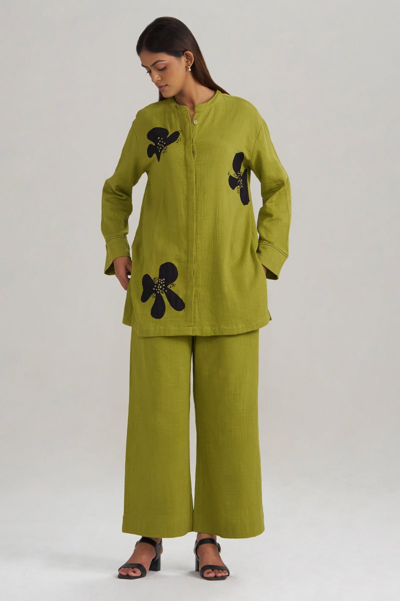 A woman modeling a matching olive green two-piece set consisting of a long-sleeve button-front tunic with black floral appliques and wide-leg trousers, photographed against a plain light gray studio background. | Lime Green Botanical Co-ord Set - Ganga Fashions