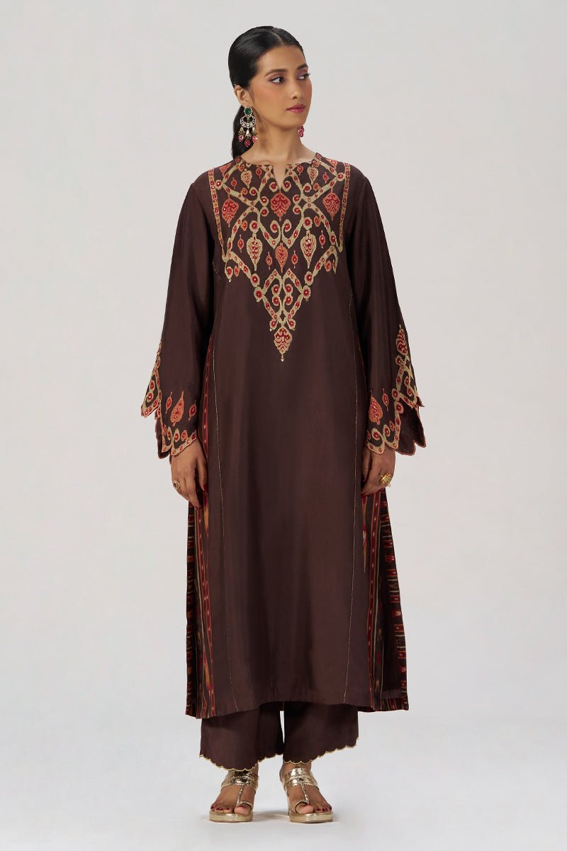 A woman modeling a dark brown traditional kurta set with intricate red, gold, and beige embroidery on the yoke and sleeve cuffs, paired with matching trousers, against a plain light gray studio background. | Deep Coffee Festive Co-ord Set - Ganga Fashions