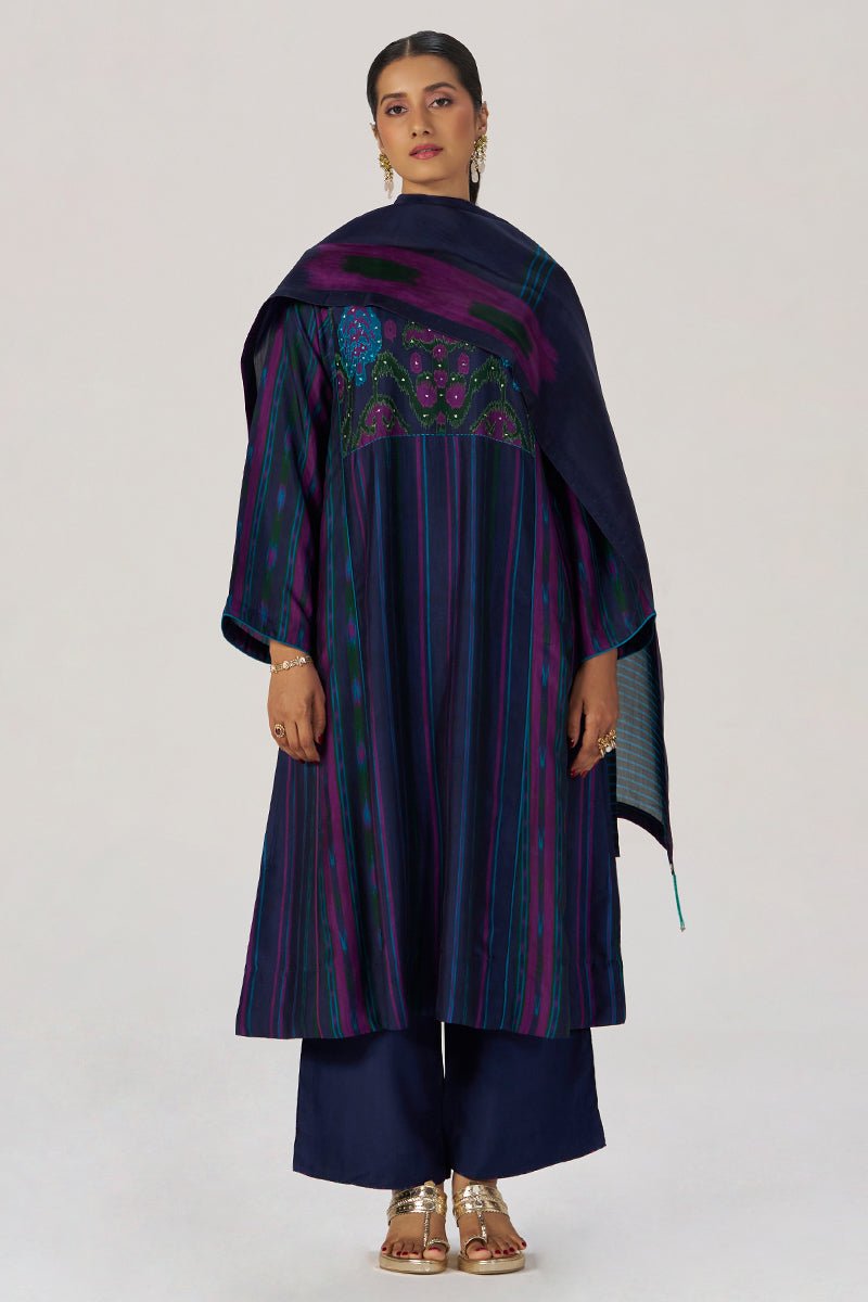A woman modeling a dark navy blue traditional outfit with vertical stripes in purple, green, and blue, featuring a matching embroidered dupatta, against a plain light gray studio background. | Medieval Blue Silk Festive Kurta Set - Ganga Fashions