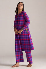 Woman wearing a purple and pink plaid outfit with floral embroidery on a plain background