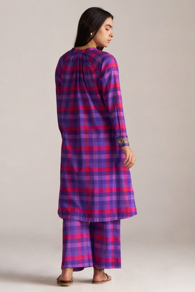 Woman wearing a purple and pink checkered outfit on a plain background