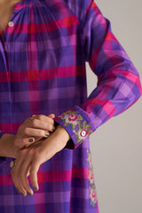 Close-up of a person wearing a purple and pink plaid shirt with floral embroidery on the sleeve.