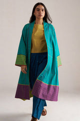 Woman wearing a long turquoise and purple coat over a yellow top and blue pants on a white background | Navigate Blue Checkard Kimono with Moss Yellow Top and Blue Bottom Co Ord Set