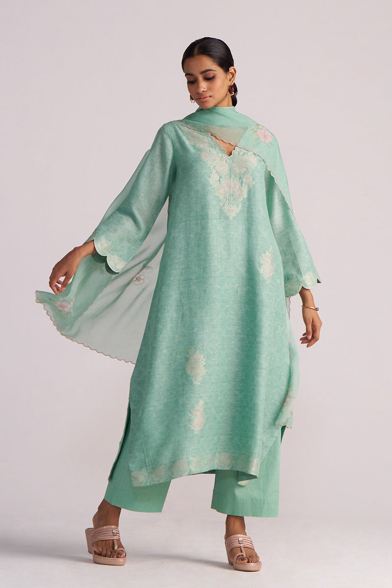 Woman wearing a Dusty Jade Green Woven Silk Kurta Set with floral patterns on a white background
