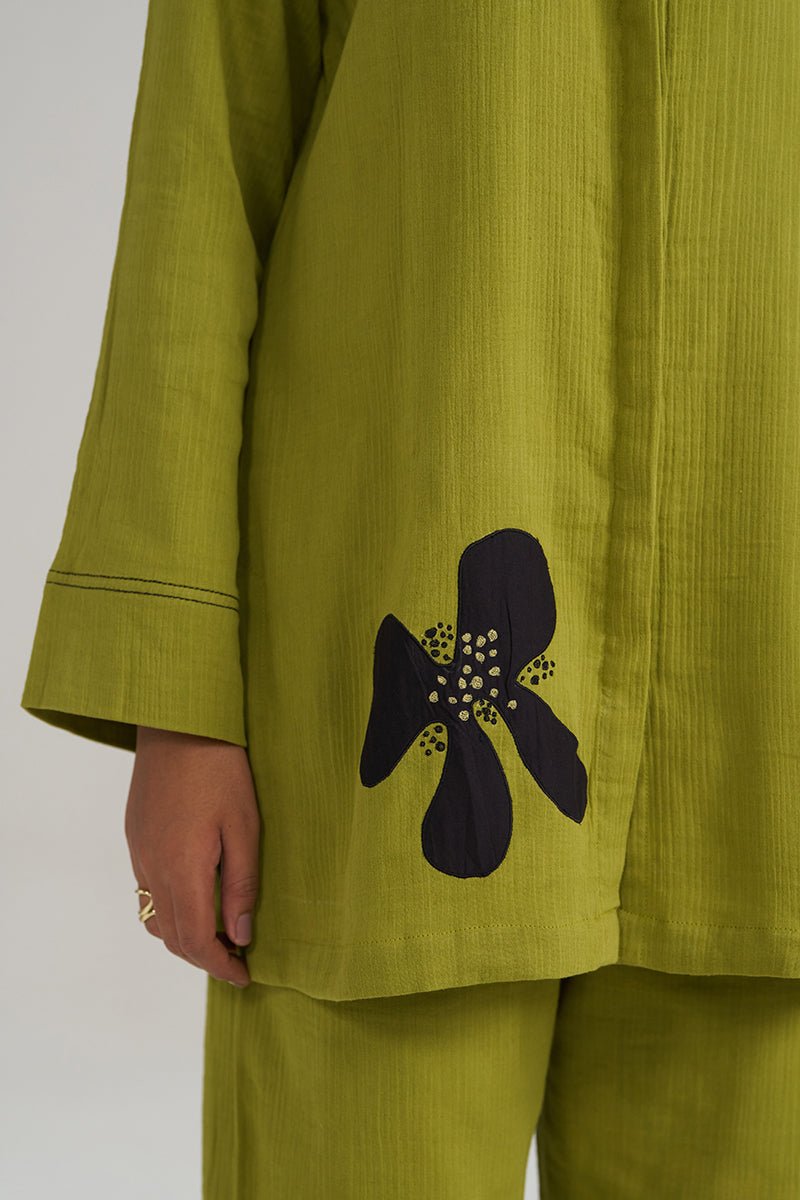 Close-up of a person wearing a textured olive green kurta or tunic with a large black floral applique on the lower front, paired with matching olive green pants. The fabric has a distinct vertical crinkle texture. | Lime Green Botanical Co-ord Set - Ganga Fashions