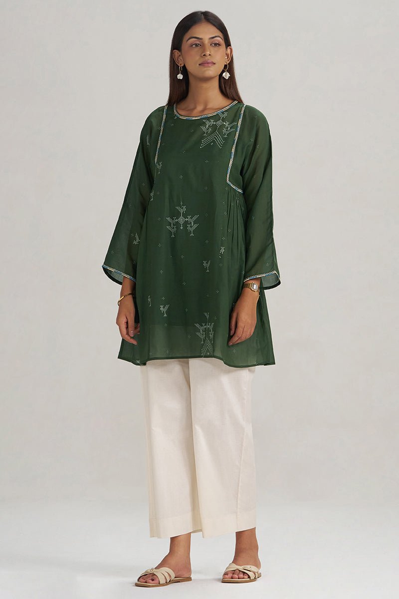 A woman modeling a dark green kurta with subtle white embroidery and white wide-leg pants against a plain light gray studio background. | Mehndi Green Hand-Printed Mul-Mul Tunic - Ganga Fashions