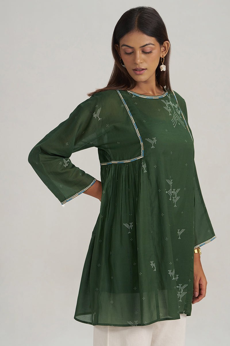 A woman modeling a dark green embroidered kurta with white floral patterns and light blue trim, paired with white pants, against a plain light gray background. | Mehndi Green Hand-Printed Mul-Mul Tunic - Ganga Fashions
