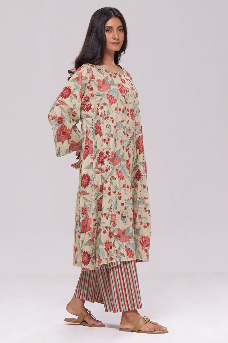A woman modeling a loose beige tunic with a red and green floral print, paired with striped pants and flat sandals, against a plain light gray studio background. | Vintage Beige and Rose Floral Print Kurta and Stripe Bottom Set - Ganga Fashions
