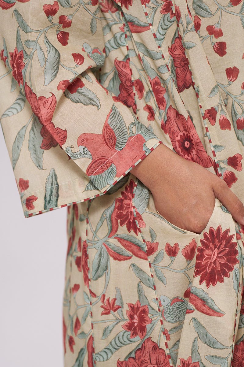 Close-up of a cream-colored cotton pajama or robe featuring a vintage-style floral and bird print in red and muted green, with a hand tucked into a side pocket. | Vintage Beige and Rose Floral Print Kurta and Stripe Bottom Set - Ganga Fashions