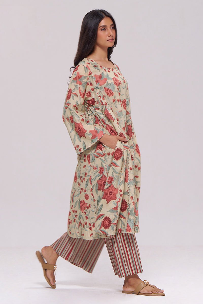 A woman modeling a long-sleeved cream-colored kurta with a red and green floral print, paired with striped pants and tan sandals, against a plain light gray studio background. | Vintage Beige and Rose Floral Print Kurta and Stripe Bottom Set - Ganga Fashions