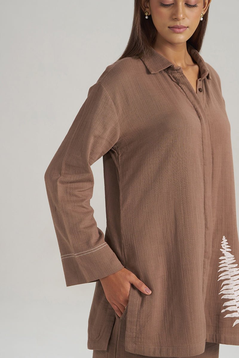 A woman wearing a brown long-sleeve button-up tunic top with a white fern leaf print on the lower right side, shown against a light gray studio background. | Chocolate and Fern Co-ord Set - Ganga Fashions