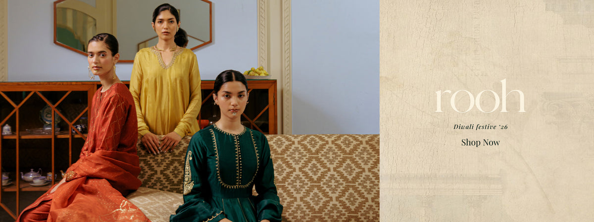 Three women modeling traditional South Asian salwar kameez in a styled indoor setting, with one in rust orange, one in mustard yellow, and one in deep teal green. The right side features a textured beige panel with the text 'rooh Diwali special 14 Shop Now'. | Rooh Collection
