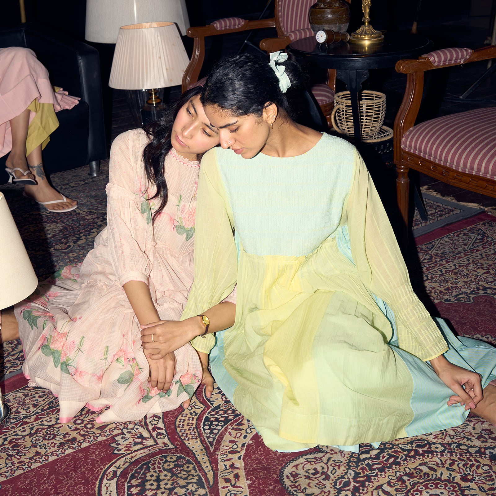 Two women in traditional attire sitting on a patterned rug in a room with furniture and decor. | rangmanch collection | elegant kurta sets & co-ords | ganga fashion